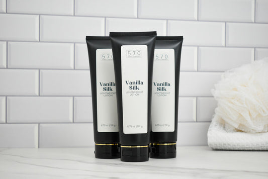 Three black and white tubes of 570 Vanilla Silk on a bathroom counter with a tiled wall background.