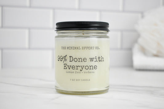 Candle jar labeled '99% Done with Everyone' by The Minimal Effort Co. on a white surface.