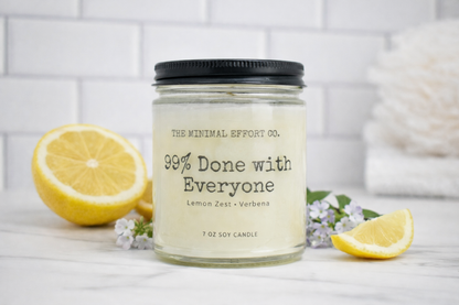 Candle jar labeled 'The Minimal Effort Co.' with lemons and flowers on a white surface.