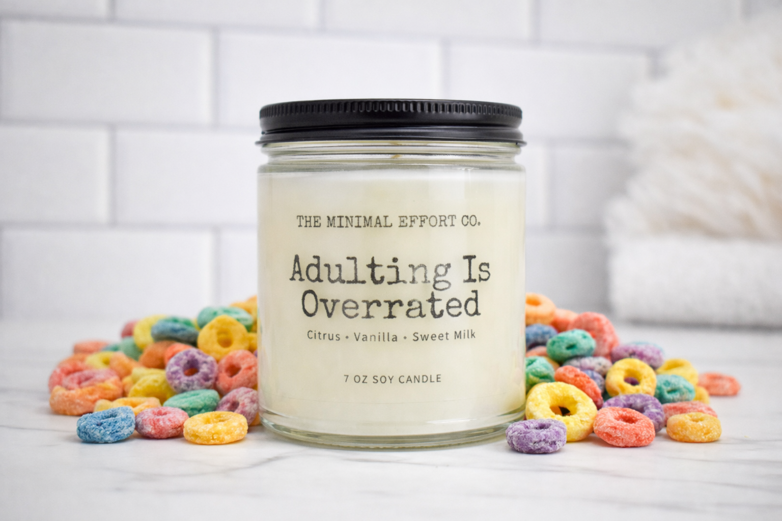 Candle labeled 'Adulting Is Overrated' surrounded by colorful cereal loops on a white background