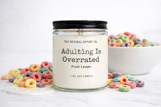 Candle labeled 'Adulting Is Overrated' with fruit loops around on a white background