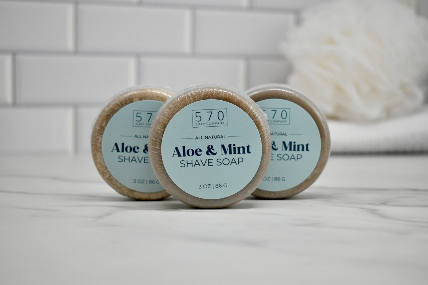 Three bars of aloe and mint shave soap on a bathroom counter with a blurred background.