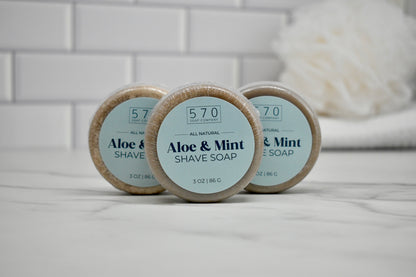 Three bars of aloe and mint shave soap on a bathroom counter with a blurred background.