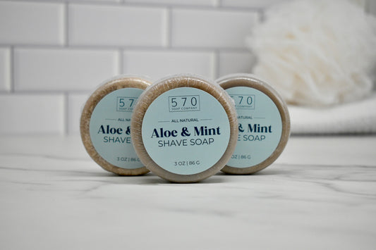 Three bars of aloe and mint shave soap on a bathroom counter with a blurred background.