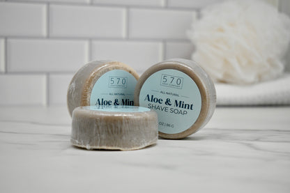 Three bars of Aloe & Mint shave soap on a bathroom counter with a tiled wall background.
