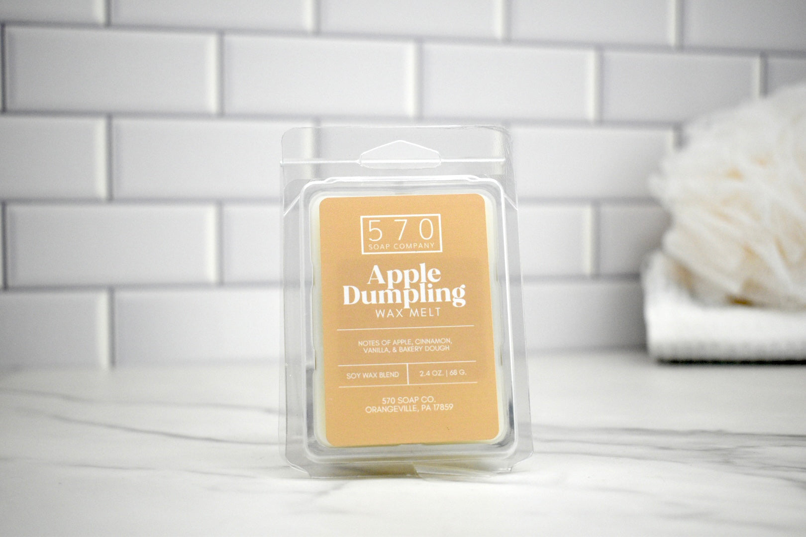 Packaged Apple Dumpling wax melt with '570' branding on a white surface with a tiled wall background