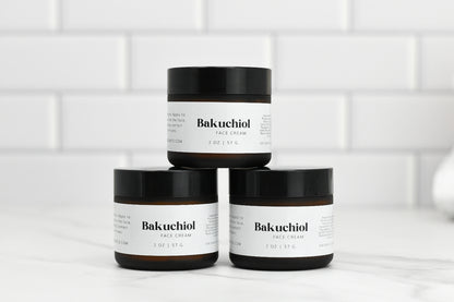 Three jars of Bakuchoil Hydrating Face Cream, a must-have for any skincare routine by 570 Soap Co., are arranged in a pyramid formation against a white tiled background. The jars come with black lids and white labels that highlight the product's ability to enhance your complexion's natural radiance.