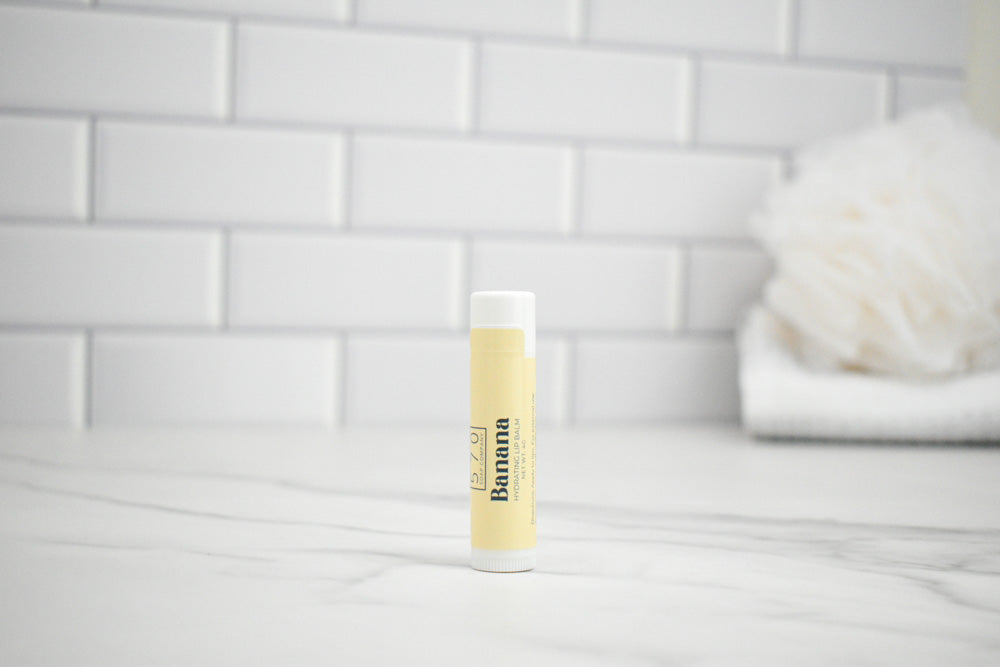 Banana lip balm on a white surface with a tiled wall background