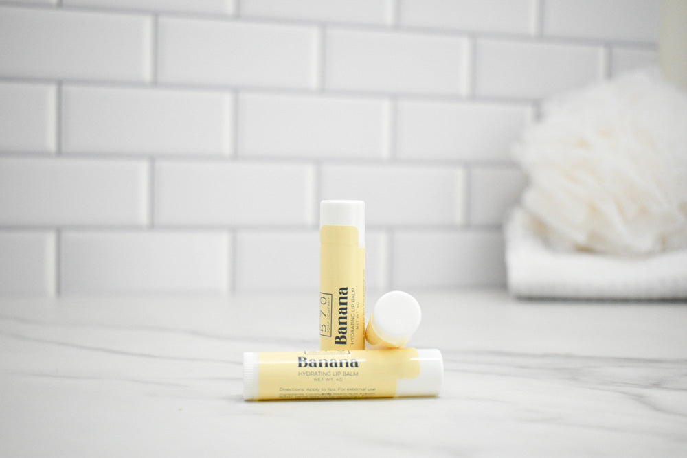 Two lip balm tubes on a white surface with a tiled wall background
