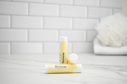 Two lip balm tubes on a white surface with a tiled wall background
