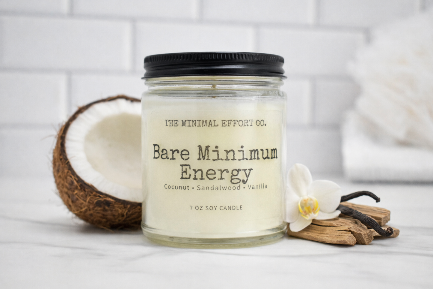 Candle labeled 'Bare Minimum Energy' from 'The Minimal Effort Co.' with coconut, vanilla bean, and orchid on a white background.