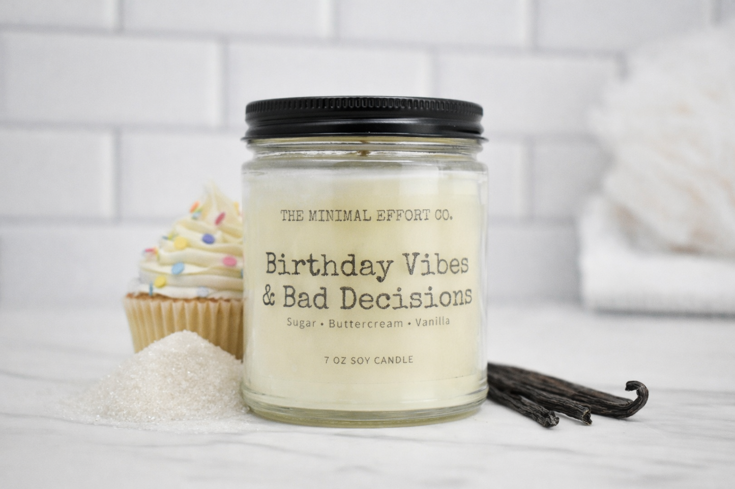 Candle labeled 'Birthday Vibes & Bad Decisions' with vanilla beans and a cupcake on a white surface.