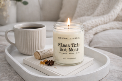 Candle labeled 'Bless This Hot Mess' on a tray with a mug of tea and decorative items.