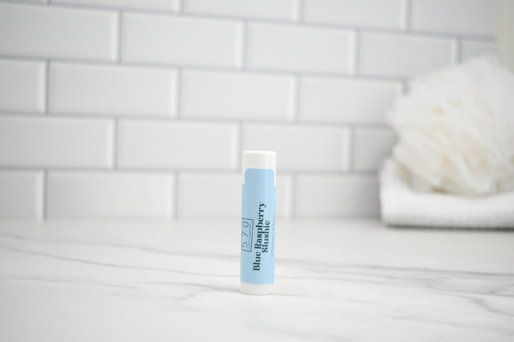 Lip balm with blue label on a white surface against a tiled wall background