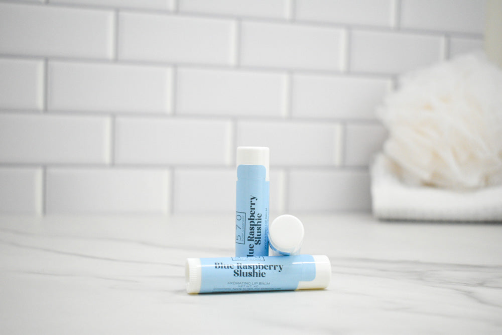 Two lip balm tubes on a bathroom counter with a tiled wall background