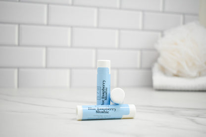 Two lip balm tubes on a bathroom counter with a tiled wall background