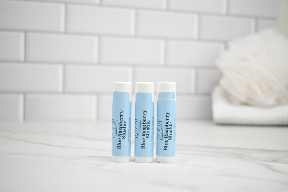 Three lip balm tubes with blue labels on a white surface with a tiled wall background