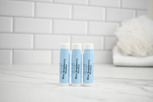 Three lip balm tubes with blue labels on a white surface with a tiled wall background