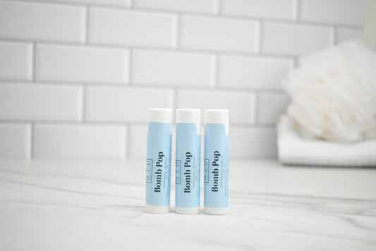 Three lip balm tubes labeled 'Bomb Pop' on a marble surface with a tiled wall background.