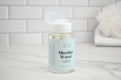 Bottle of Micellar Water with a white cap on a marble surface with a tiled wall background
