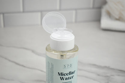Bottle of micellar water with a white cap on a marble surface.