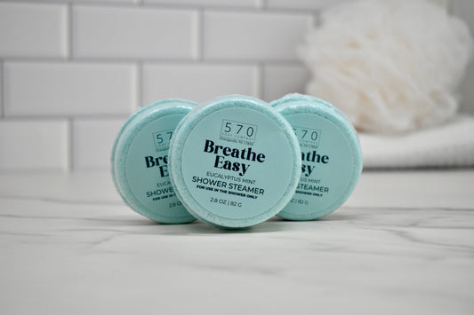 Three 'Breathe Easy' shower steamer containers on a bathroom counter.