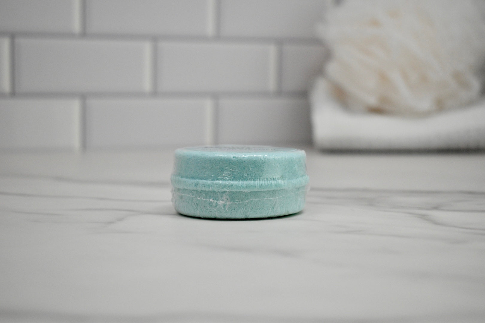 Light blue bath bomb on a white surface with a blurred bathroom background