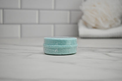 Light blue bath bomb on a white surface with a blurred bathroom background