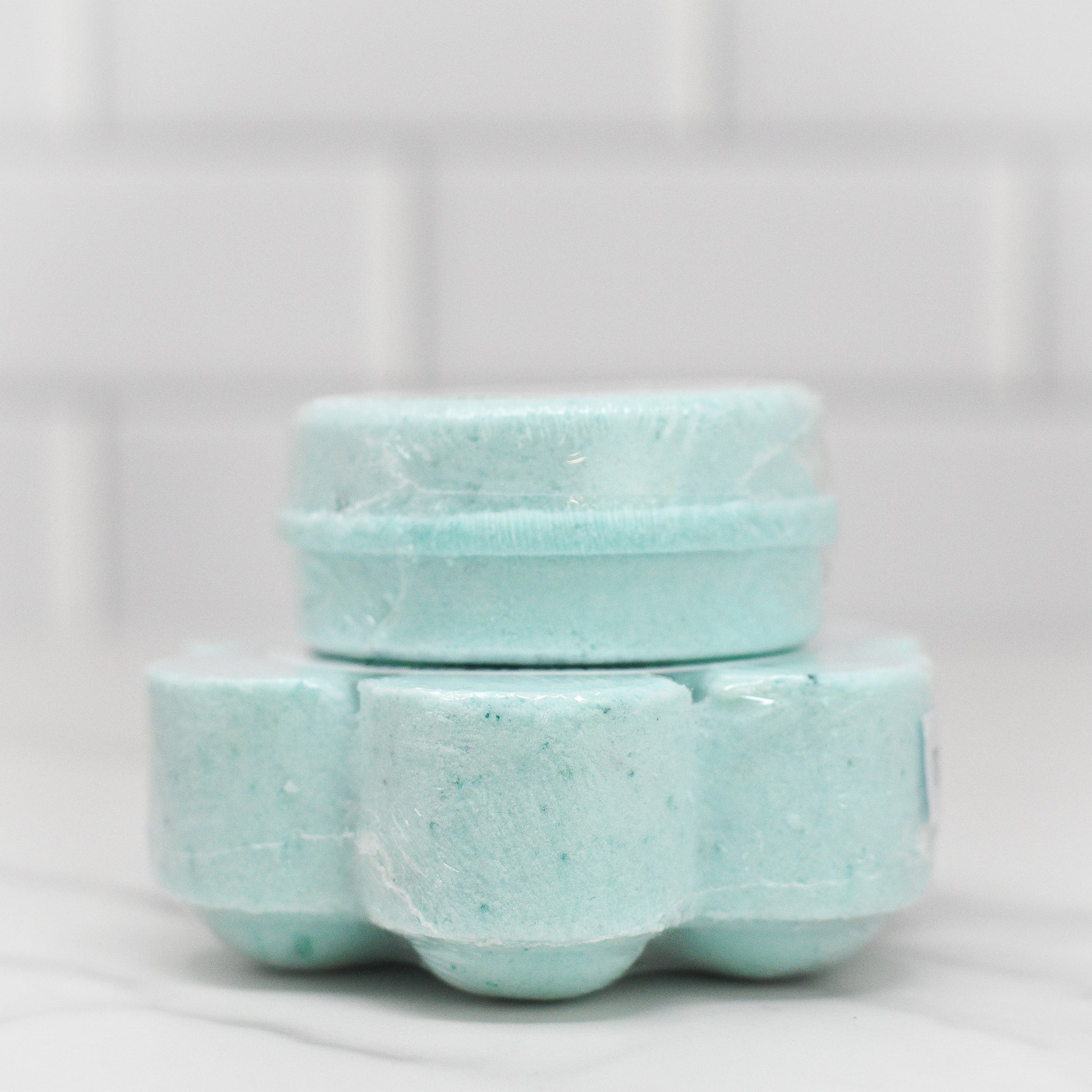 A collection of Breathe Easy Shower Steamers from 570 Soap Co., infused with Eucalyptus Mint for a refreshing aromatic experience, is arranged on a white marble surface against a tiled backdrop. Each steamer is individually wrapped in clear plastic.