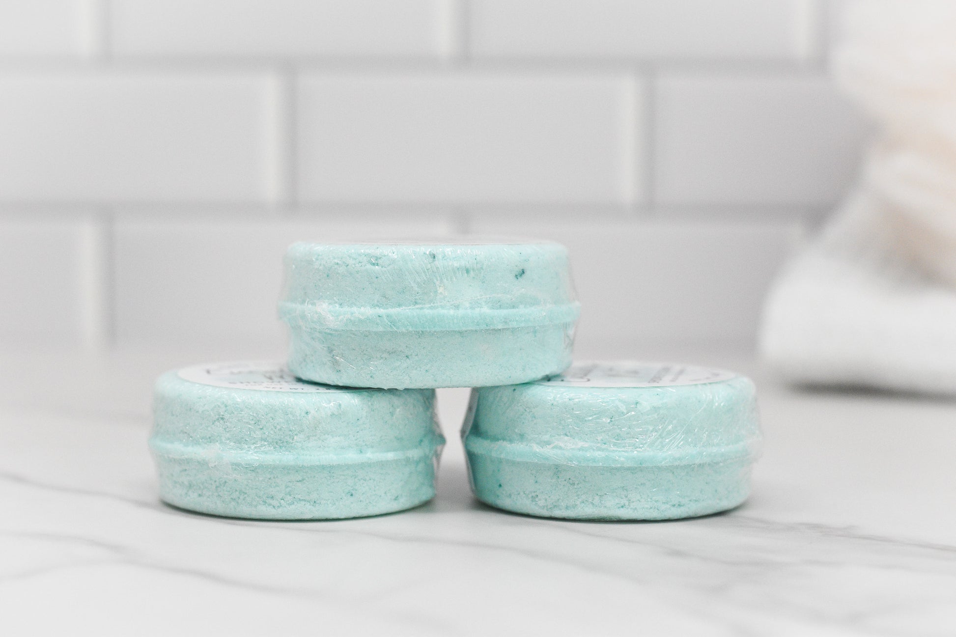 A trio of Breathe Easy Shower Steamers by 570 Soap Co., in a relaxing eucalyptus mint fragrance, is neatly arranged on a white marble surface with a backdrop of white tiles.