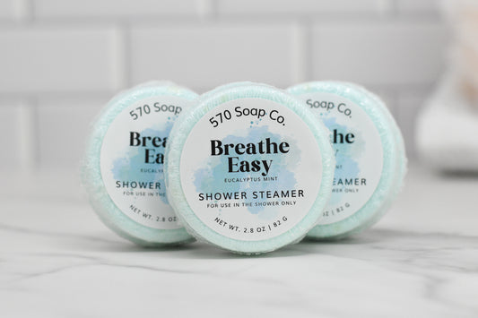 Aromatic, mint-colored round shower steamers by 570 Soap Co., labeled "Breathe Easy," promise an invigorating experience against a white tiled background. Each steamer, featuring the eucalyptus mint scent, weighs 2.8 oz (82 g).