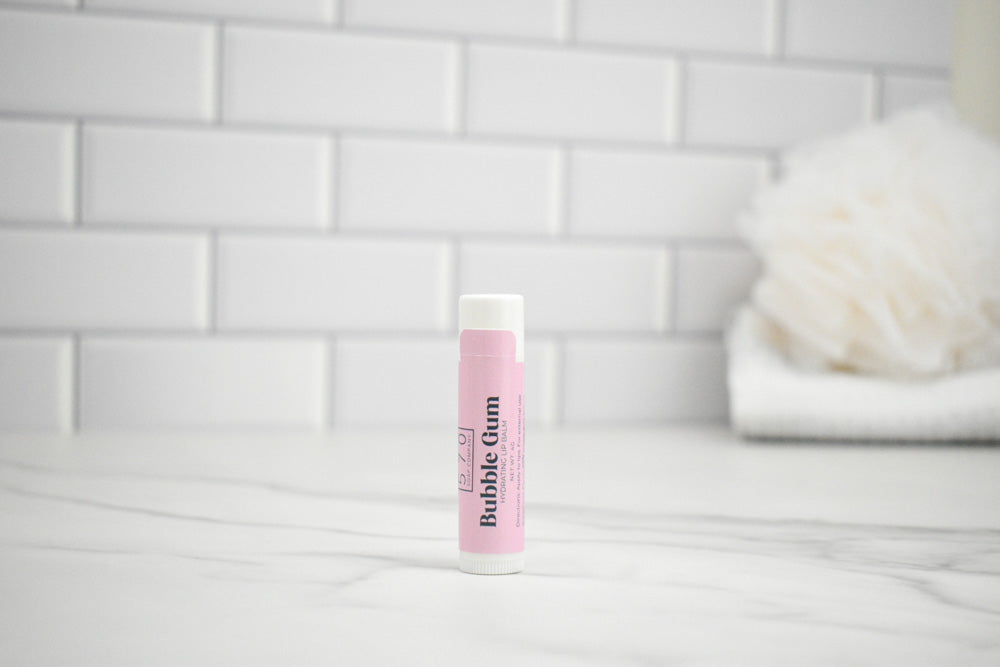 Lip balm with a pink label on a white surface against a tiled wall background