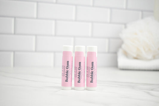 Three lip balm tubes labeled 'Bubble Gum' on a white surface with a tiled wall background.