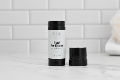 A Bug-Be-Gone Lotion Stick by 570 Soap Co. sits on a marble surface against a white tile backdrop, showcasing its efficacy as a bug repellent. The black container is open, highlighting the all-natural contents, and the product weighs 2 oz (57 g), proudly emphasizing its natural ingredients.