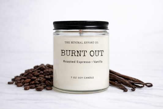 Candle labeled 'Burnt Out' with coffee beans and vanilla pods on a white background