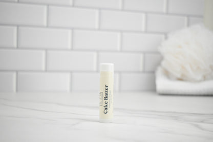 Bottle of cake batter lip balm on a white surface with a tiled wall background