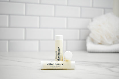 Two lip balm tubes labeled 'Cake Batter' on a white surface with a tiled wall background.