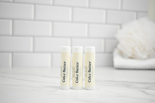 Three tubes of cake butter on a white surface with a tiled wall background