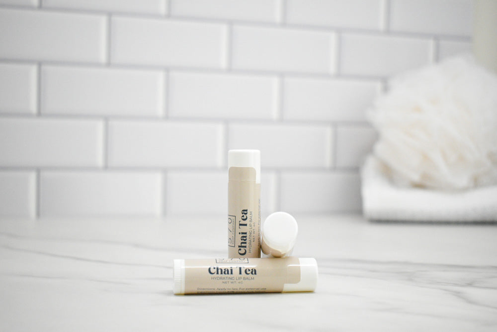 Two lip balm sticks labeled 'Chai Tea' on a white surface with a tiled wall background.