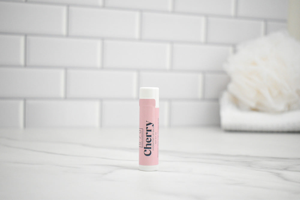 Lip balm labeled 'Cherry' on a white surface with a tiled wall background