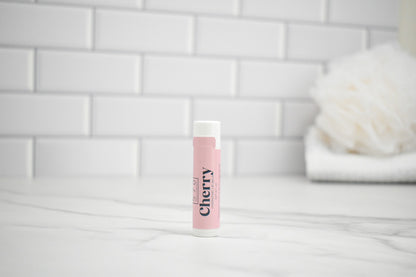 Lip balm labeled 'Cherry' on a white surface with a tiled wall background
