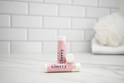 Two pink lip balms labeled 'Cherry' on a white surface with a tiled wall background.
