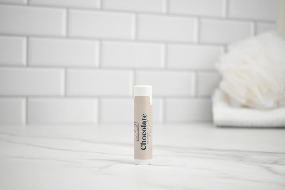 Lip Balm tube labeled 'Chocolate' on a bathroom counter with a tiled wall background