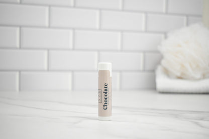 Lip Balm tube labeled 'Chocolate' on a bathroom counter with a tiled wall background
