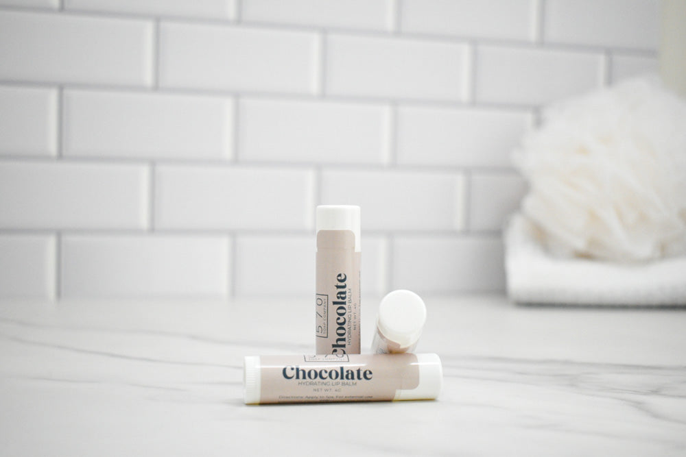 Two lip balm sticks with 'Chocodote' branding on a white surface with a tiled wall background.