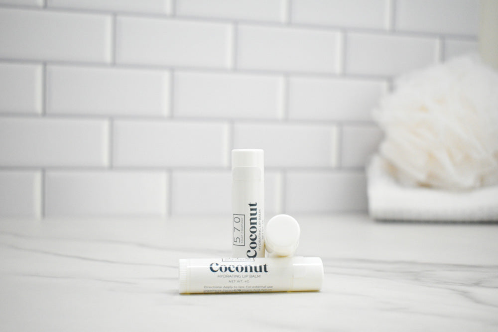 Two lip balms labeled 'Coconut' on a white surface with a tiled wall background