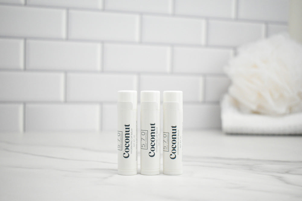 Three lip balm tubes labeled 'Coconut' on a white surface with a tiled wall background.