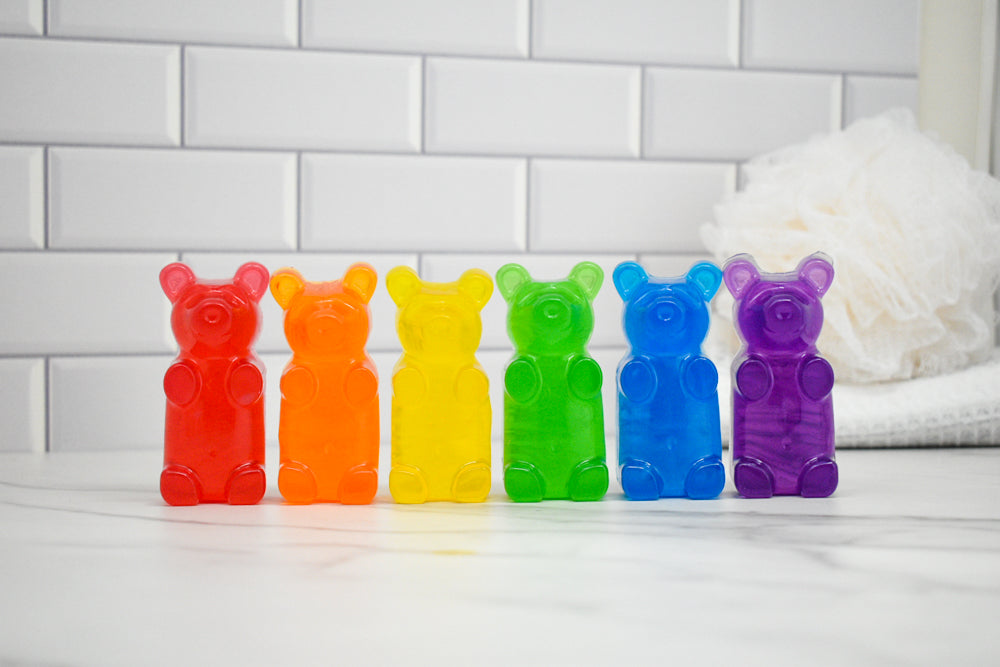 Colorful gummy bear-shaped soap in a row on a white surface with a tiled wall background.