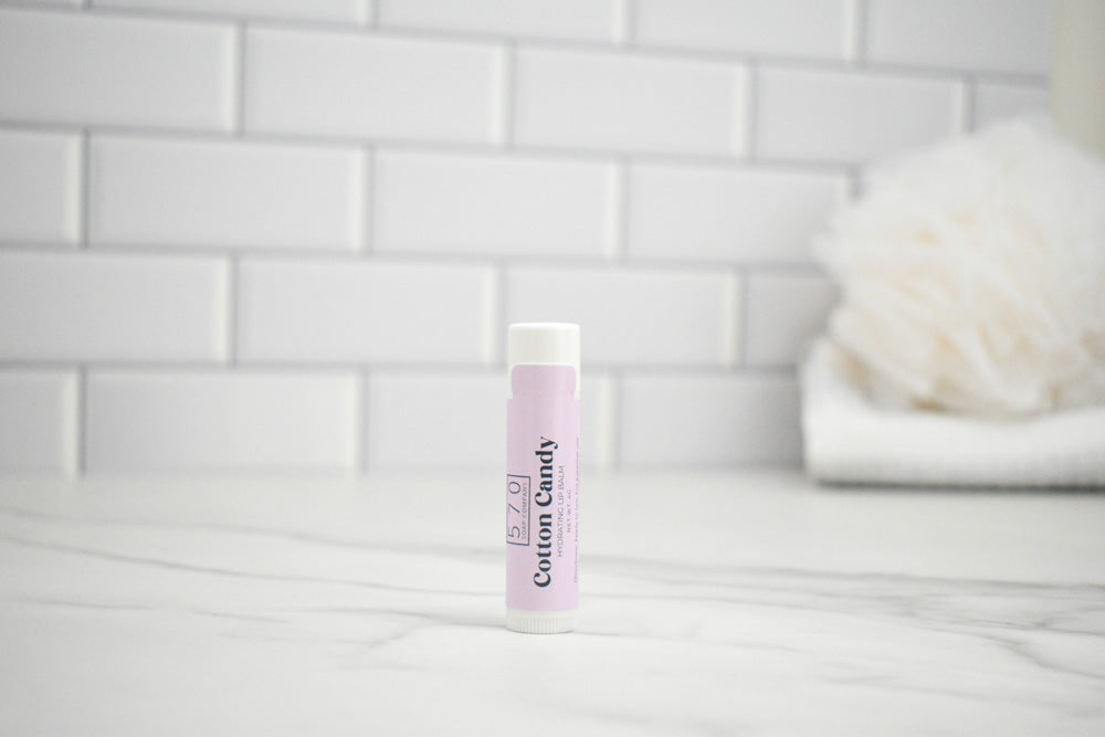 Lip balm with a label sayin "Cotton Candy" on a white surface against a tiled wall background