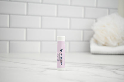 Lip balm with a label sayin "Cotton Candy" on a white surface against a tiled wall background